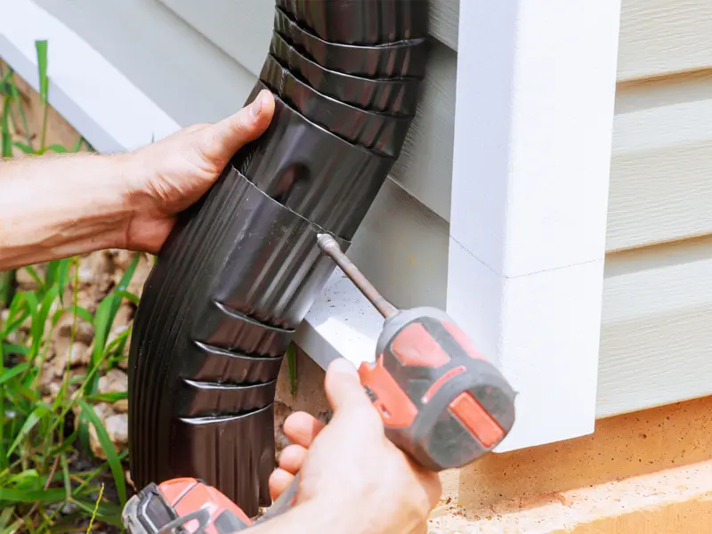 seamless gutter downspout being installed on side of home